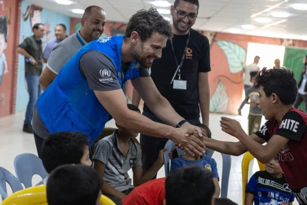 Theo James saluda a un niño sirio refugiado en un centro comunitario en el campamento de refugiados de Azraq, en Jordania, en julio de 2023. © ACNUR/Andy Hall