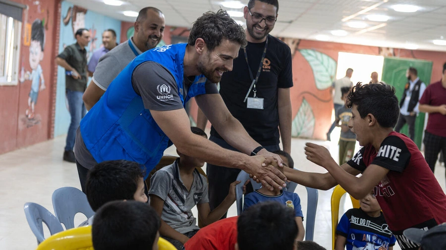 Theo James saluda a un niño sirio refugiado en un centro comunitario en el campamento de refugiados de Azraq, en Jordania, en julio de 2023. © ACNUR/Andy Hall